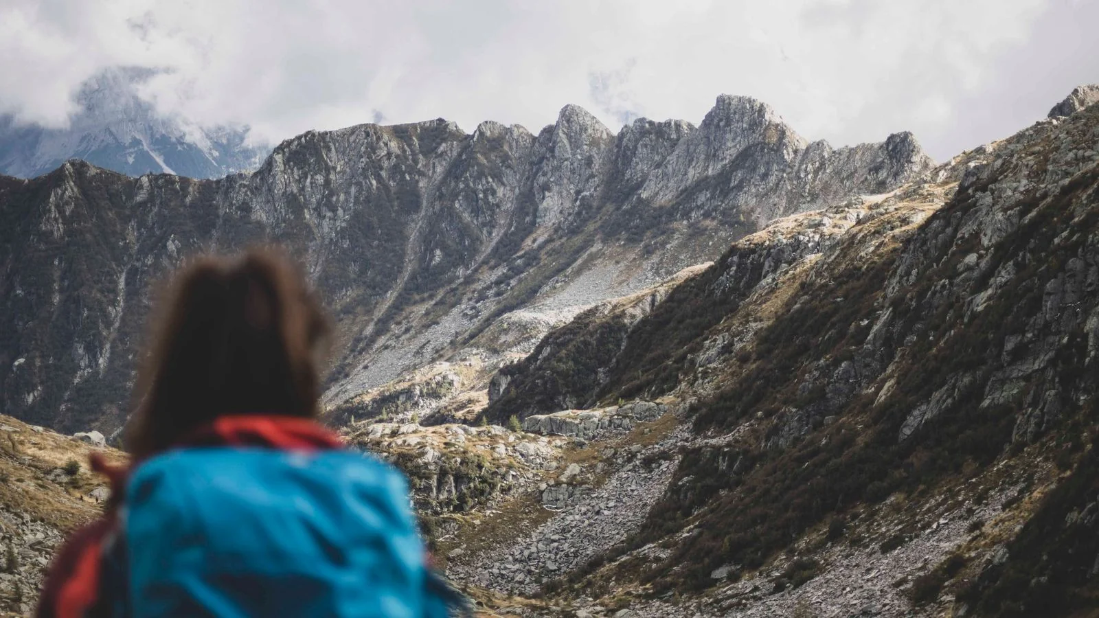 Solo hiker with a pack working across rocky alpine terrain toward a distant ridge