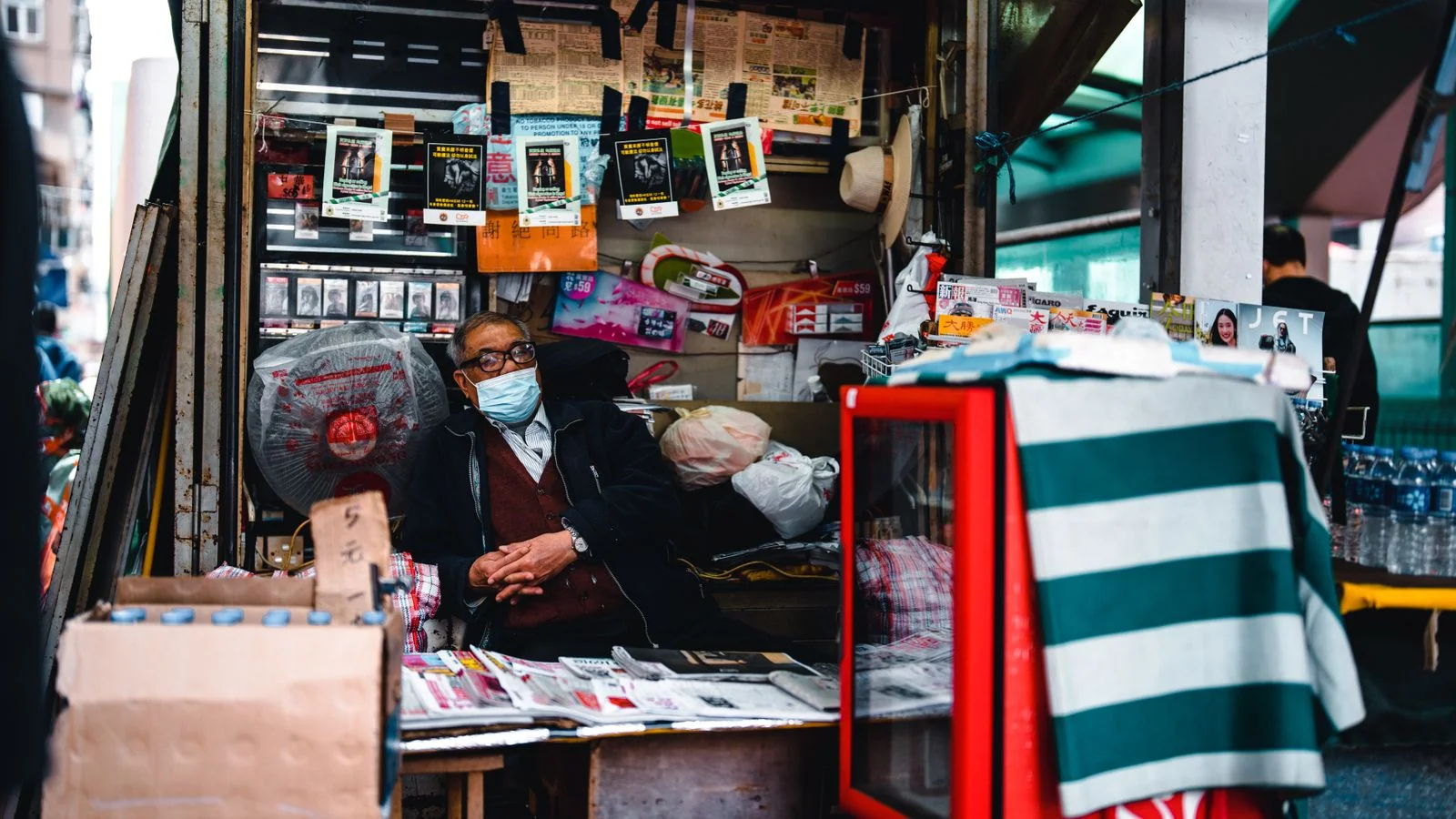 Busy urban newsstand with a vendor managing stacks of newspapers and magazines
