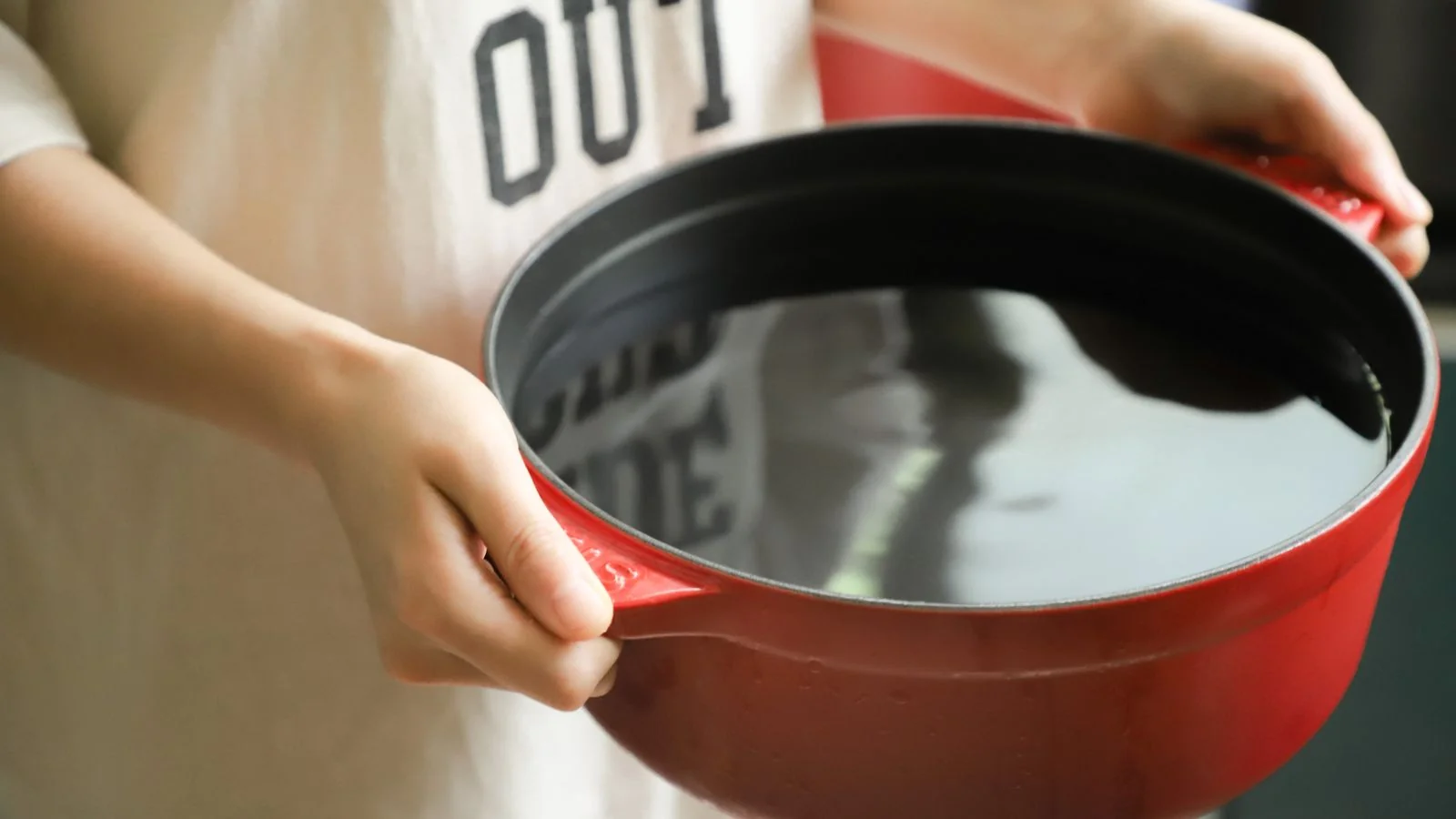 Hands holding a red pot in a home kitchen, the everyday cooking Parade readers look up