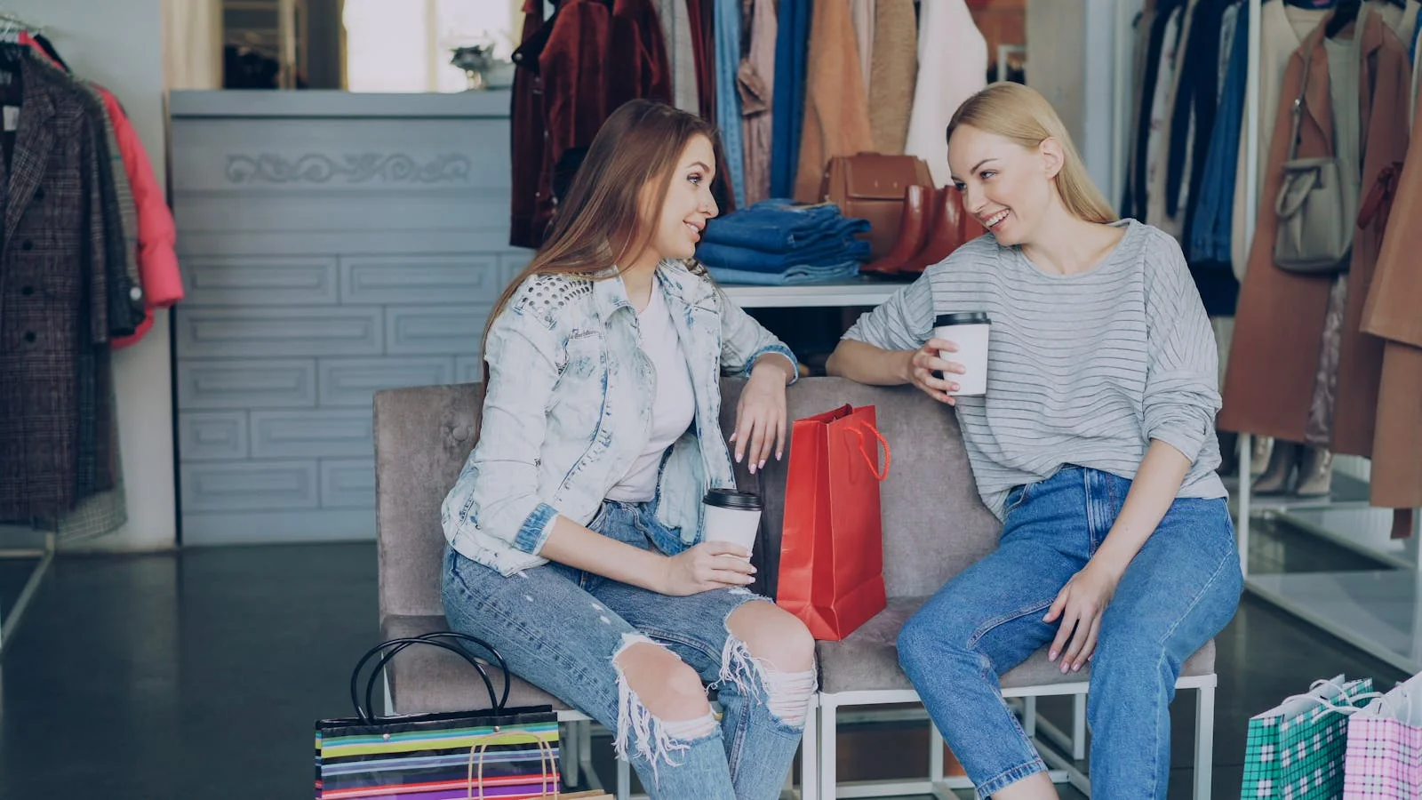 Two women in a boutique enjoying a coffee break while browsing clothing