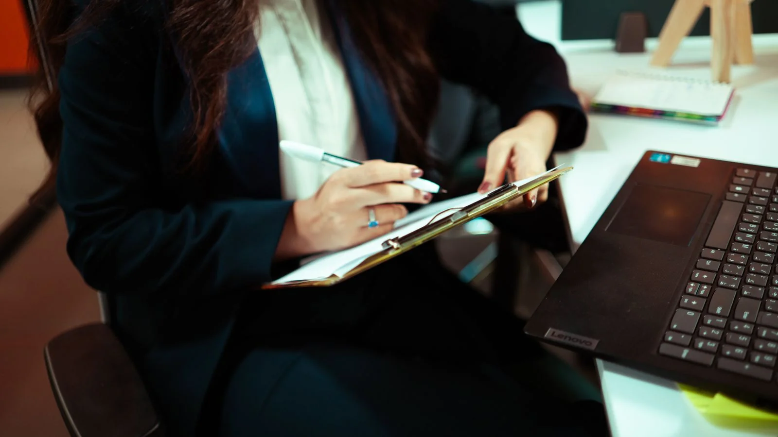 Professional writing notes on a clipboard beside a laptop, the way a trade reporter works through a pitch