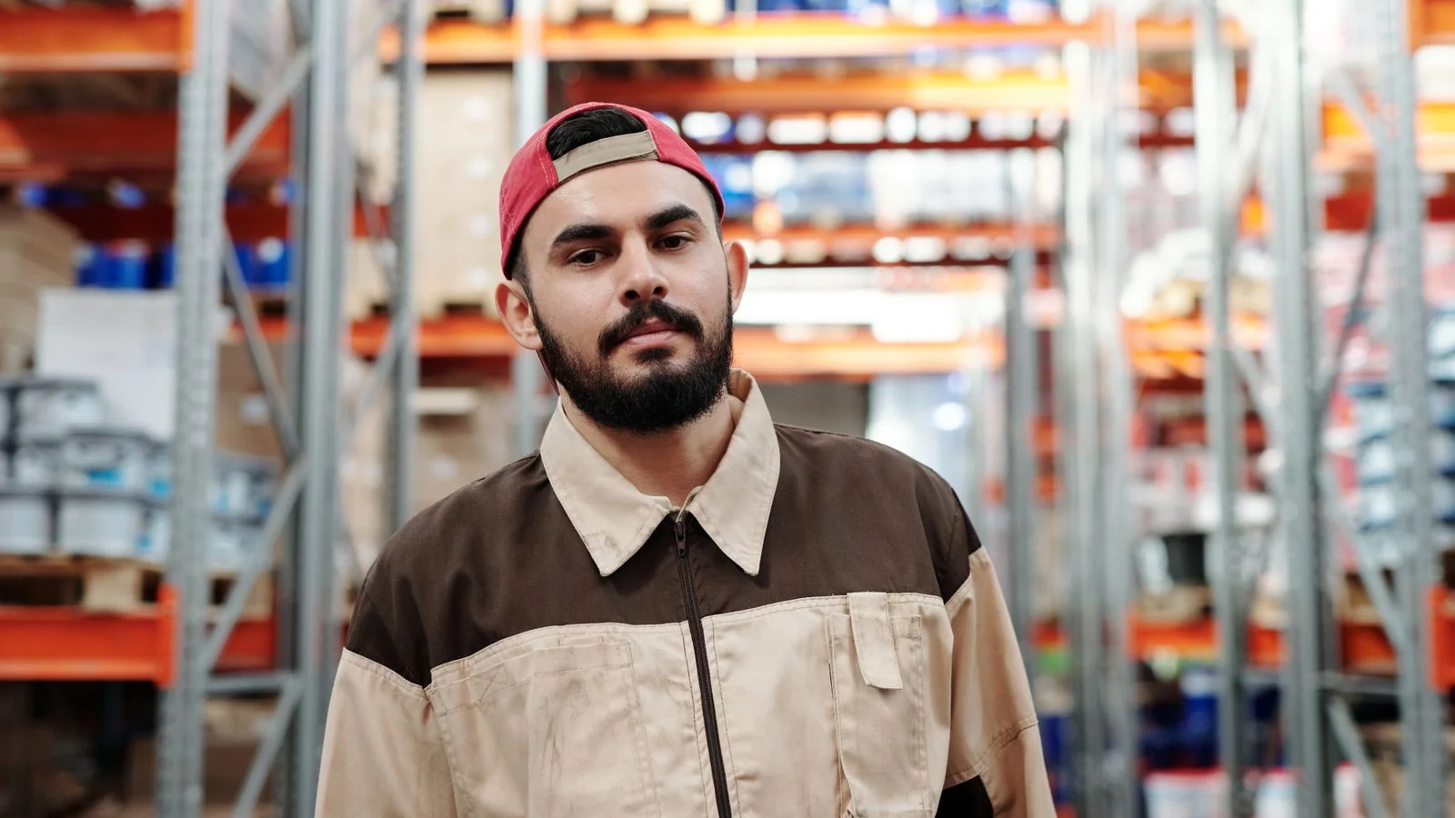 Warehouse worker in uniform standing among stacked inventory, the operations side retail trade press covers