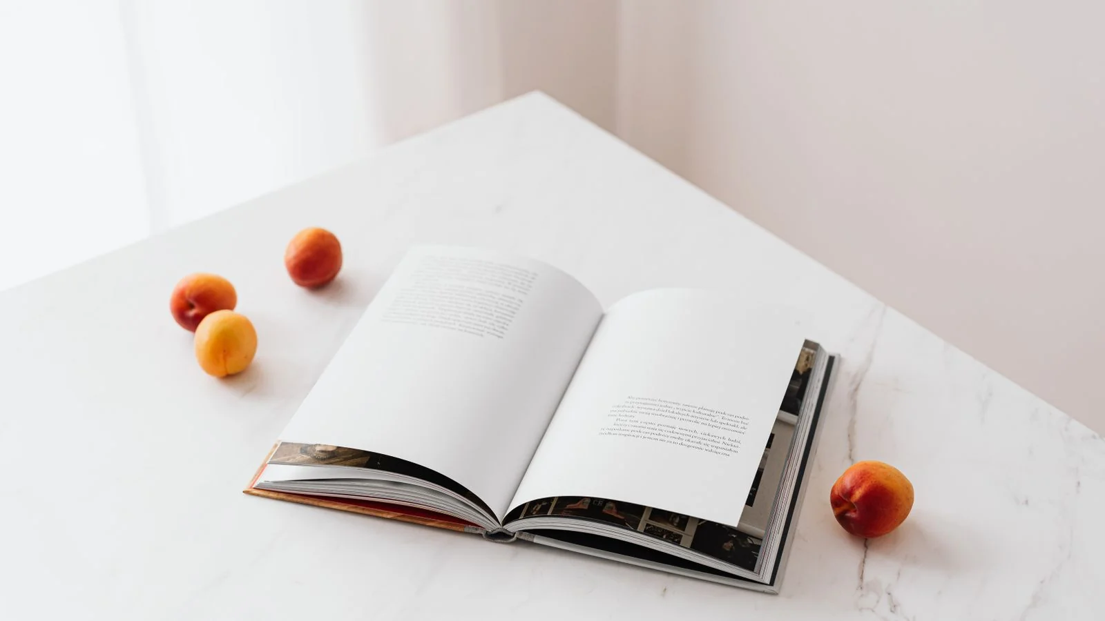 An open illustrated book on a white table beside fresh apricots