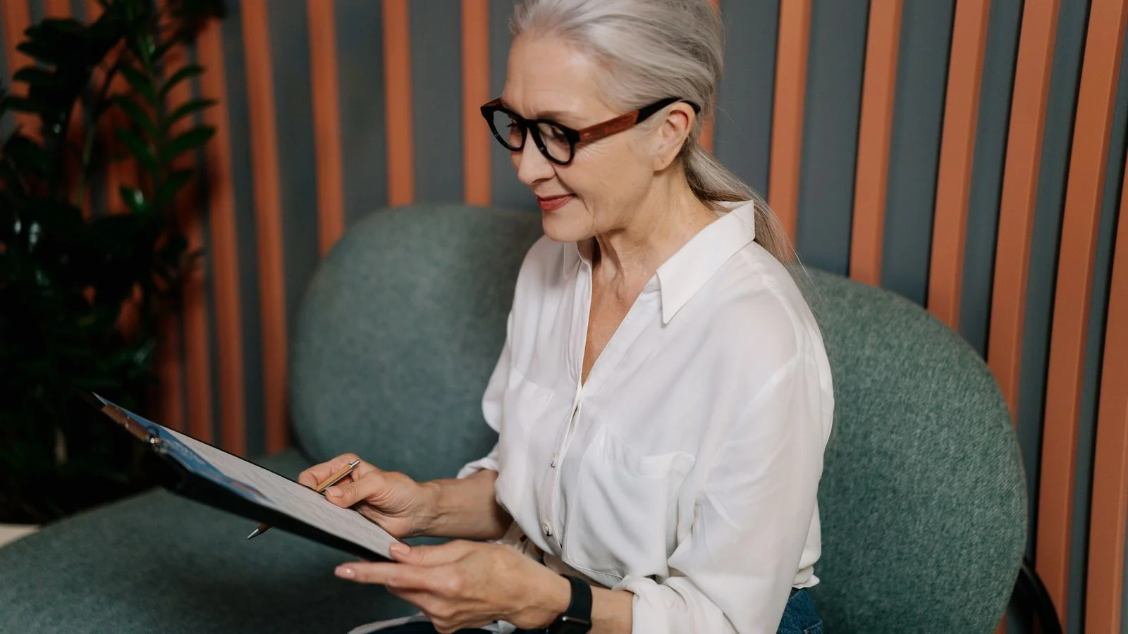 HR professional in glasses reviewing documents on a clipboard with a focused expression