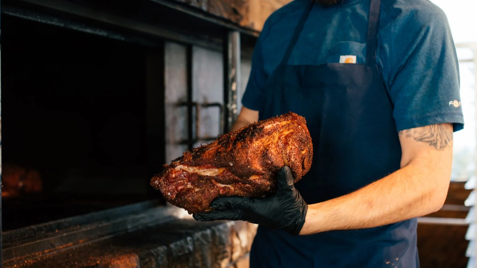 Pitmaster holding seasoned meat beside a barbecue smoker, the kind of restaurant the South's Best ballot rewards
