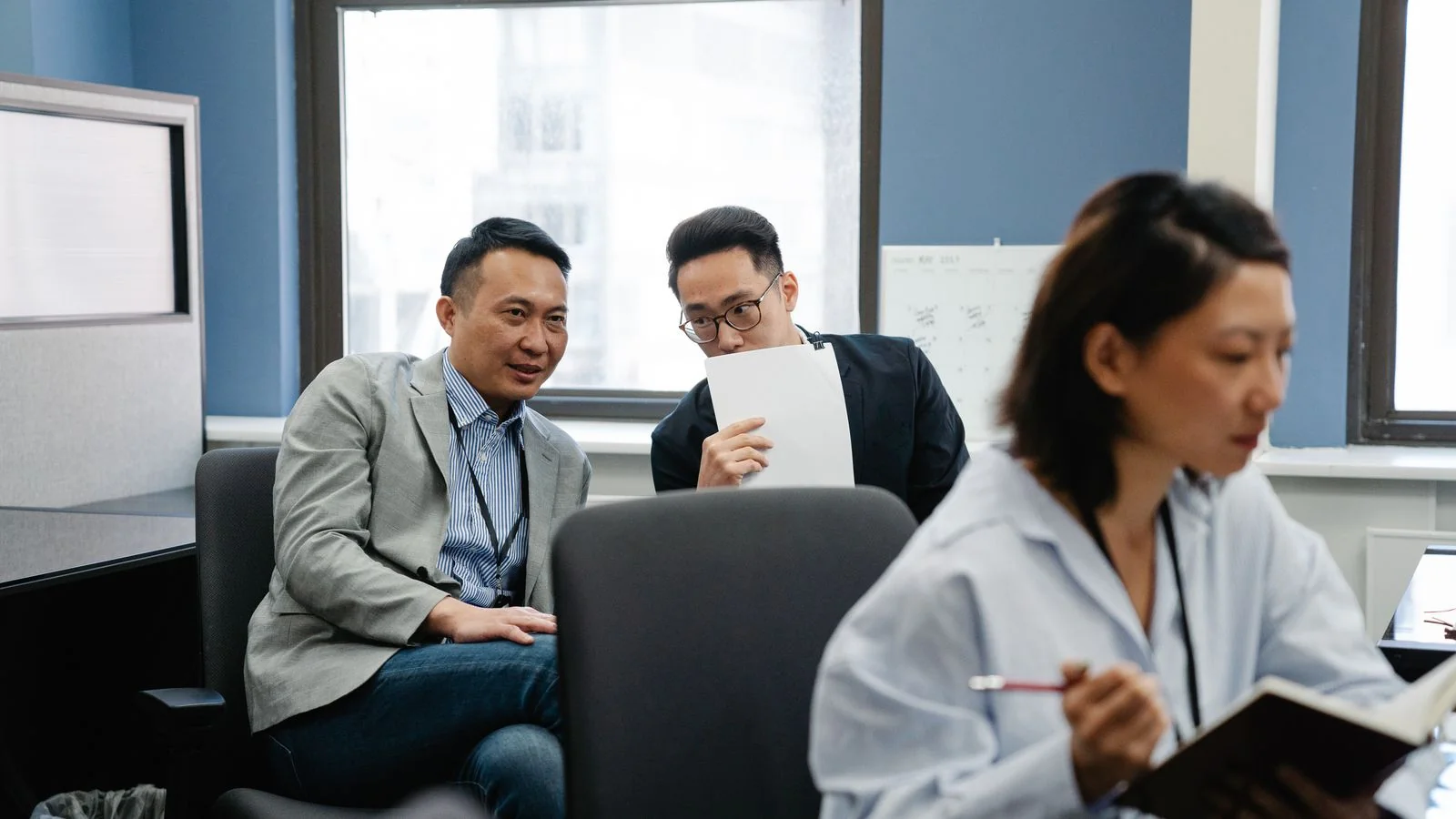 Two colleagues talking at their desks in a busy newsroom-style office