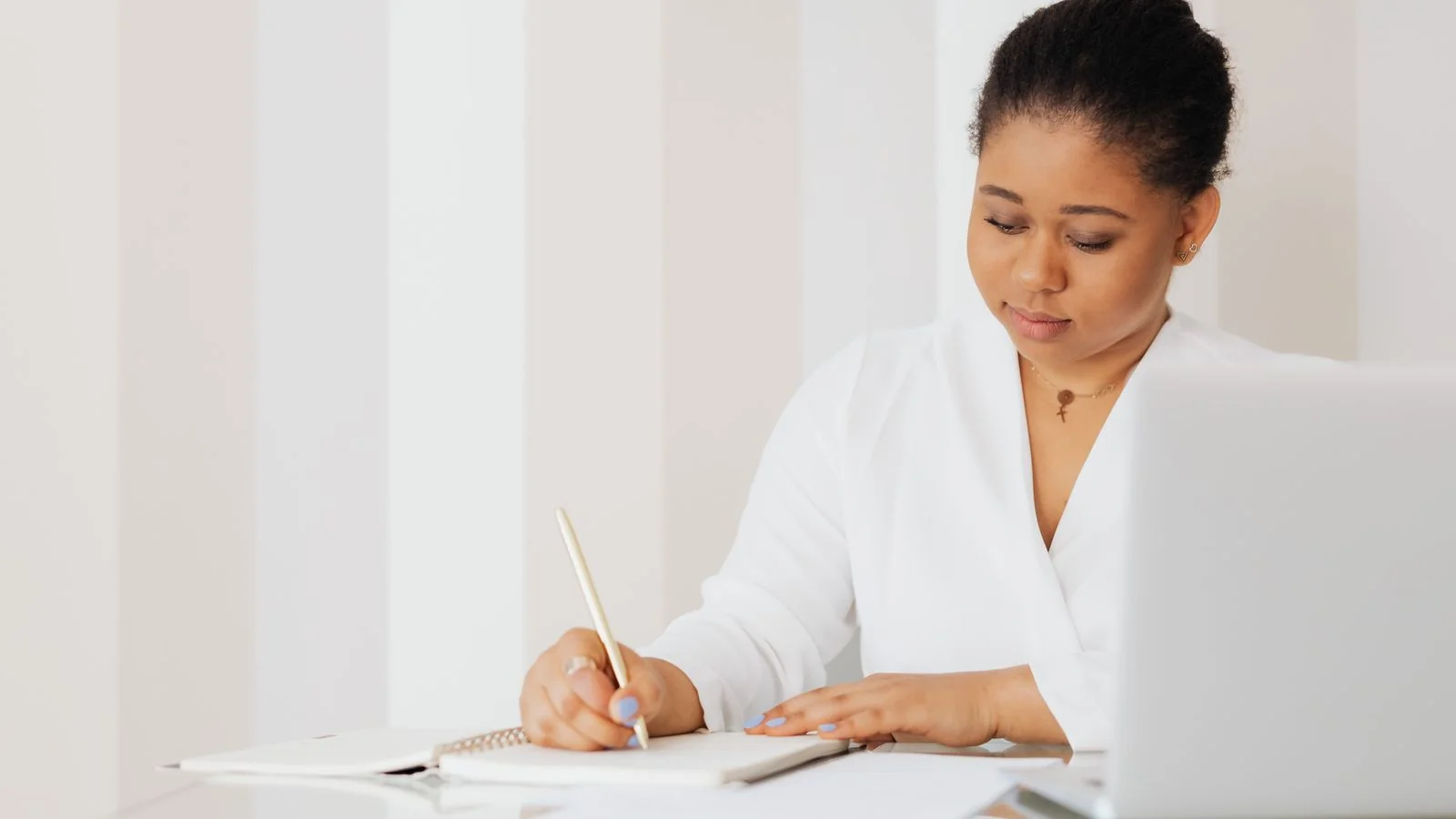 Woman writing notes at a desk with a laptop, scoring a story against a test