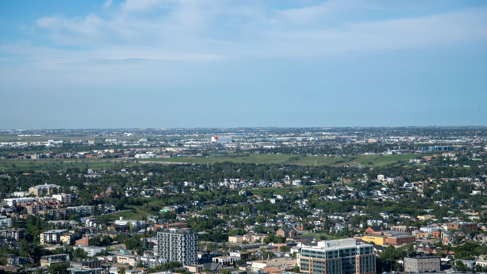 Wide aerial view of a sprawling city of buildings and green space under a bright sky
