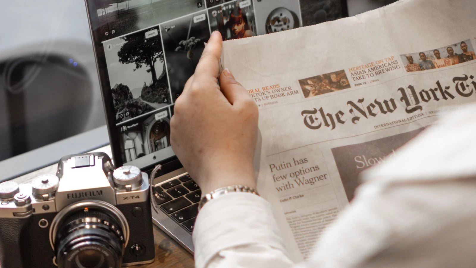 A person reading a financial newspaper beside a laptop, tracking the live market moments TheStreet covers