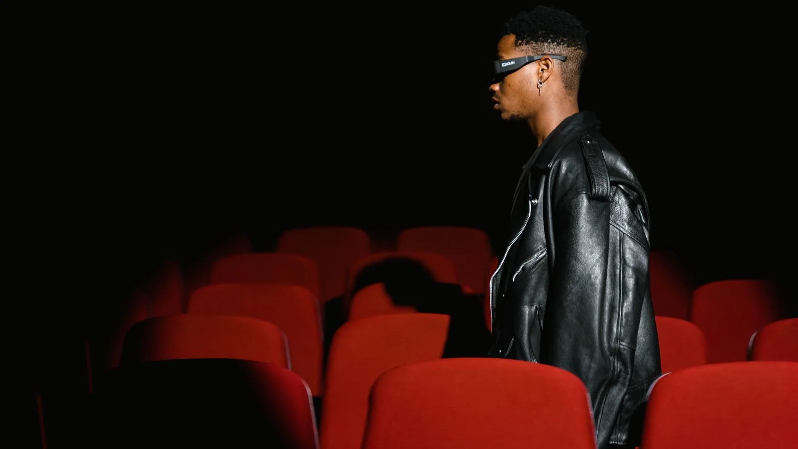 A man walking through a dim movie theater with red seats before a screening or premiere