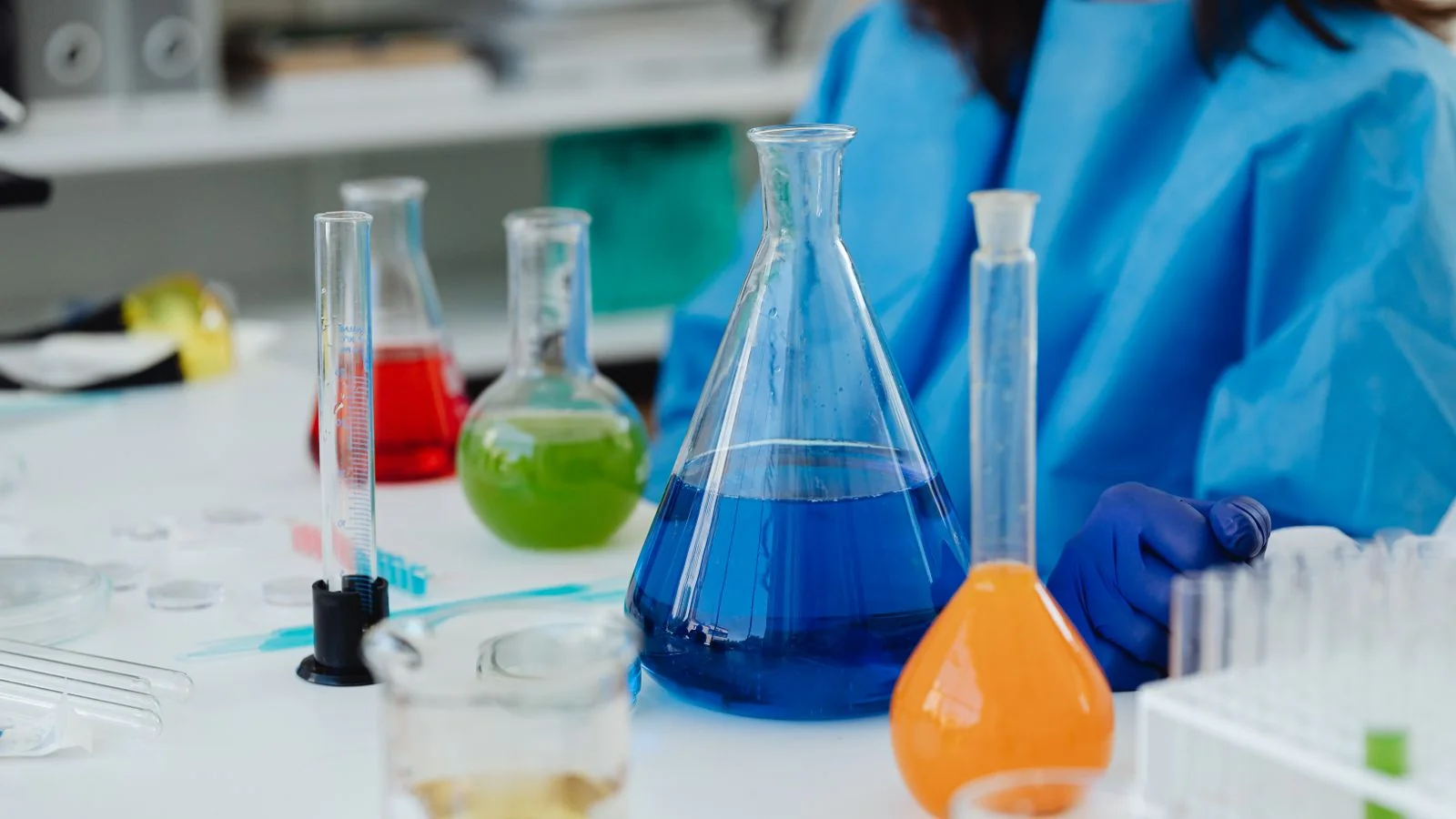 Researcher in protective gear at a laboratory bench with glassware, the cosmetic chemist credential beauty desks want