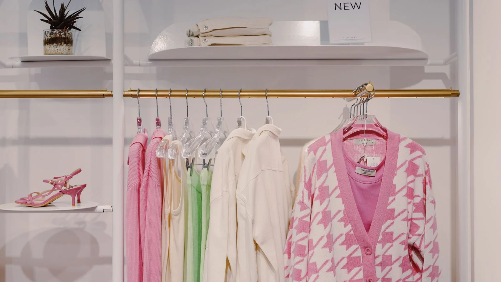 Clothing rack in a boutique showroom with a pink cardigan and green dress