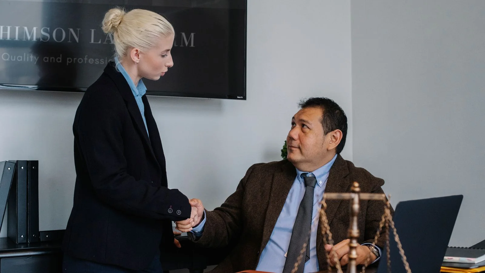 Attorneys shaking hands across a conference table with a brass scale of justice in the foreground