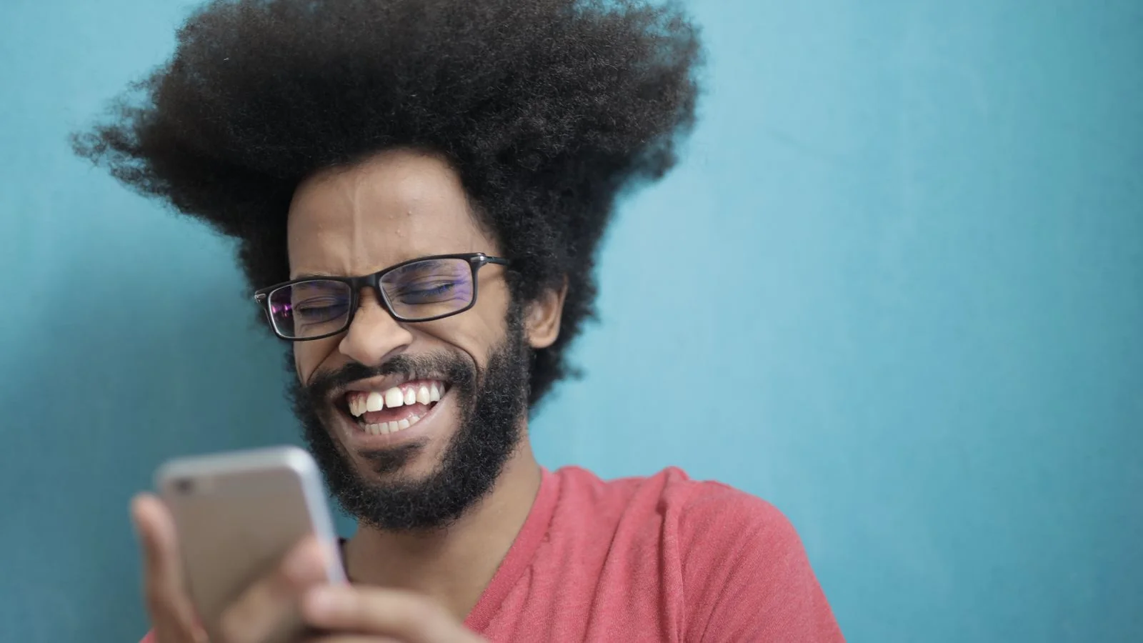 Man in glasses laughing while reading something on his phone