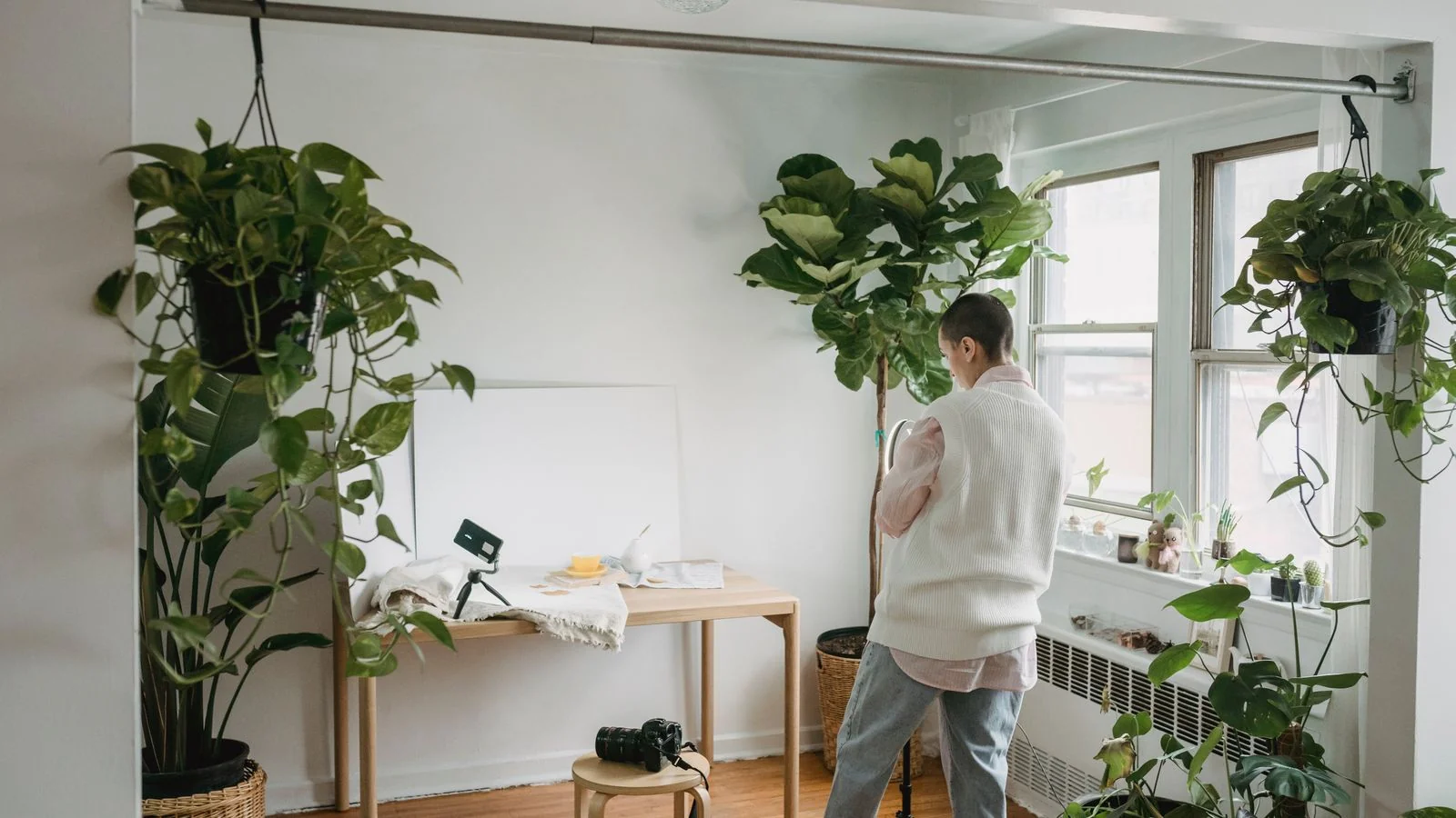 A photographer with short hair setting up a ring light in a plant-filled studio, the kind of real photography Apartment Therapy house tours require