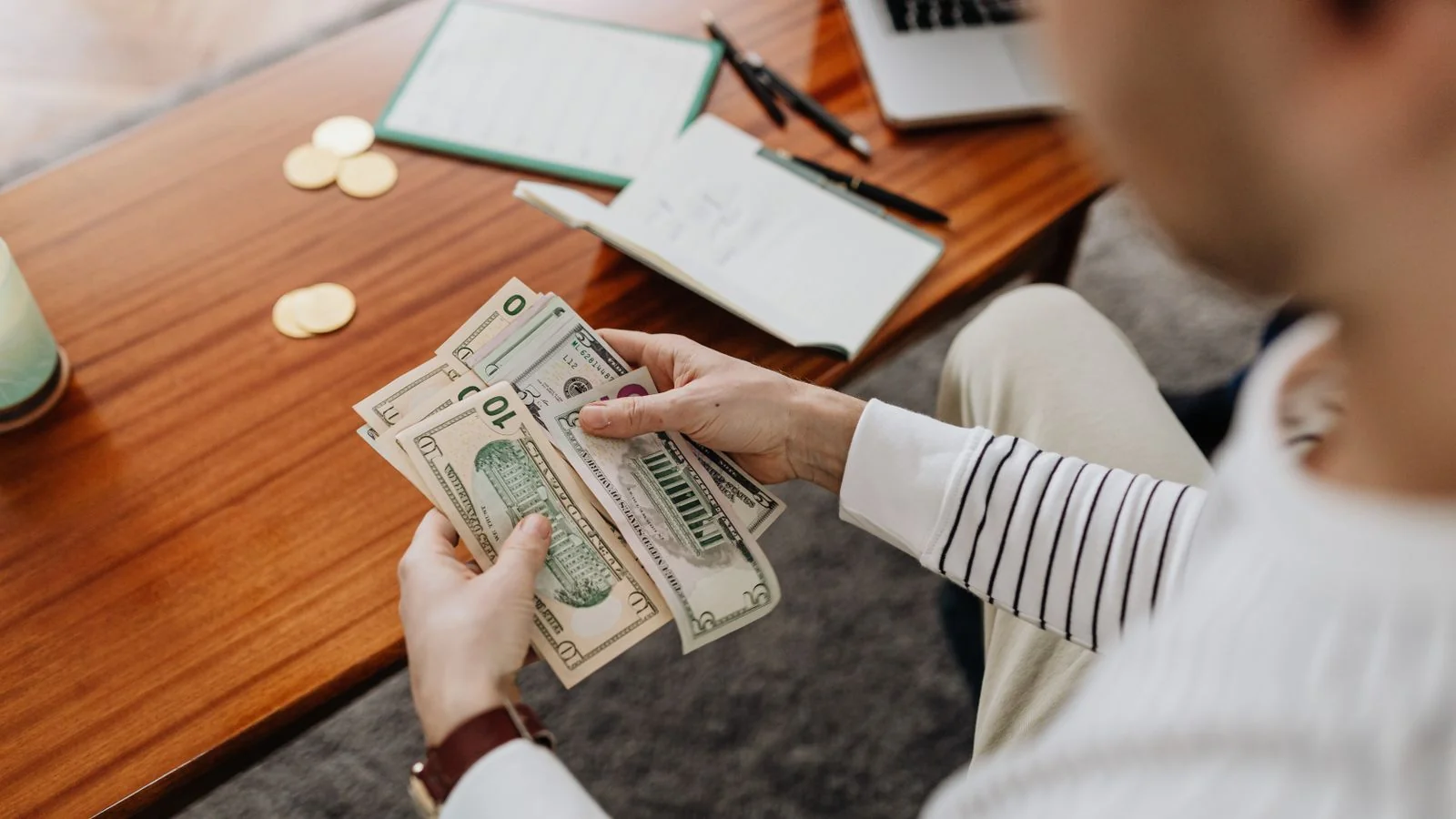 Hands counting US dollar bills beside a notebook and coins, the reseller market built on a free submission process