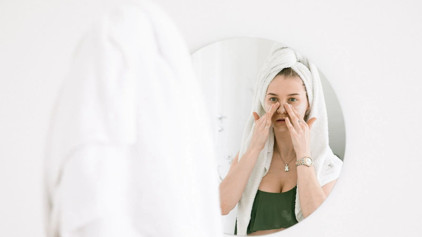 Woman applying skincare in front of a bathroom mirror, the reader question every Byrdie piece answers