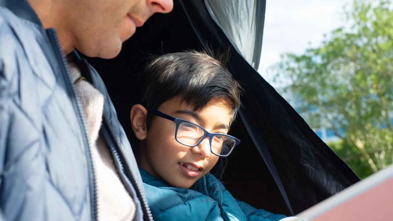 Father and son reading a book together inside a camping tent