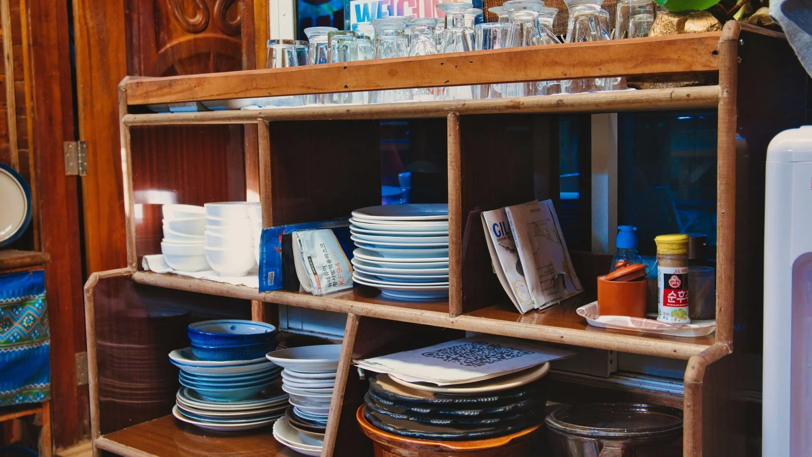 Wooden kitchen shelf holding stacked dishes, glasses, and condiment jars, like the Food52 shop's home goods