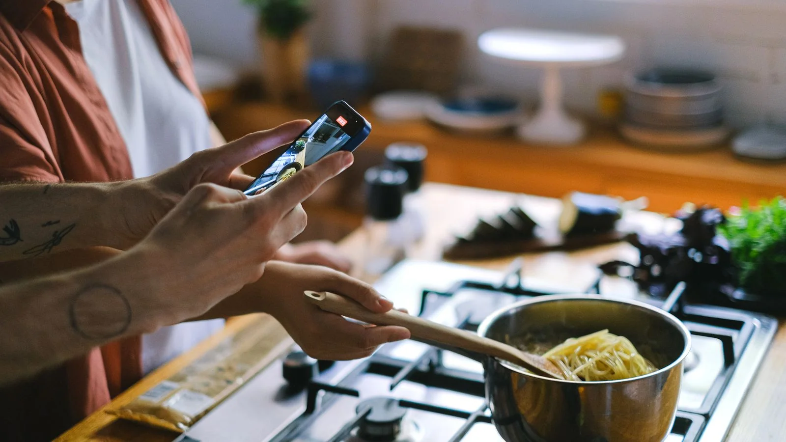 Couple cooking spaghetti in a home kitchen while filming on a phone, the way Food52 community cooks share recipes