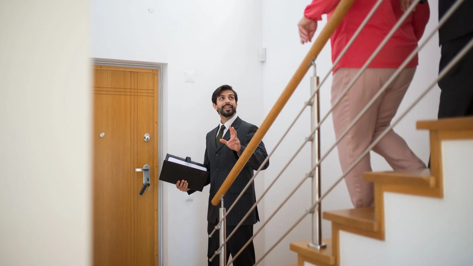 Real estate agent giving a house tour to prospective buyers on the stairs of a modern home