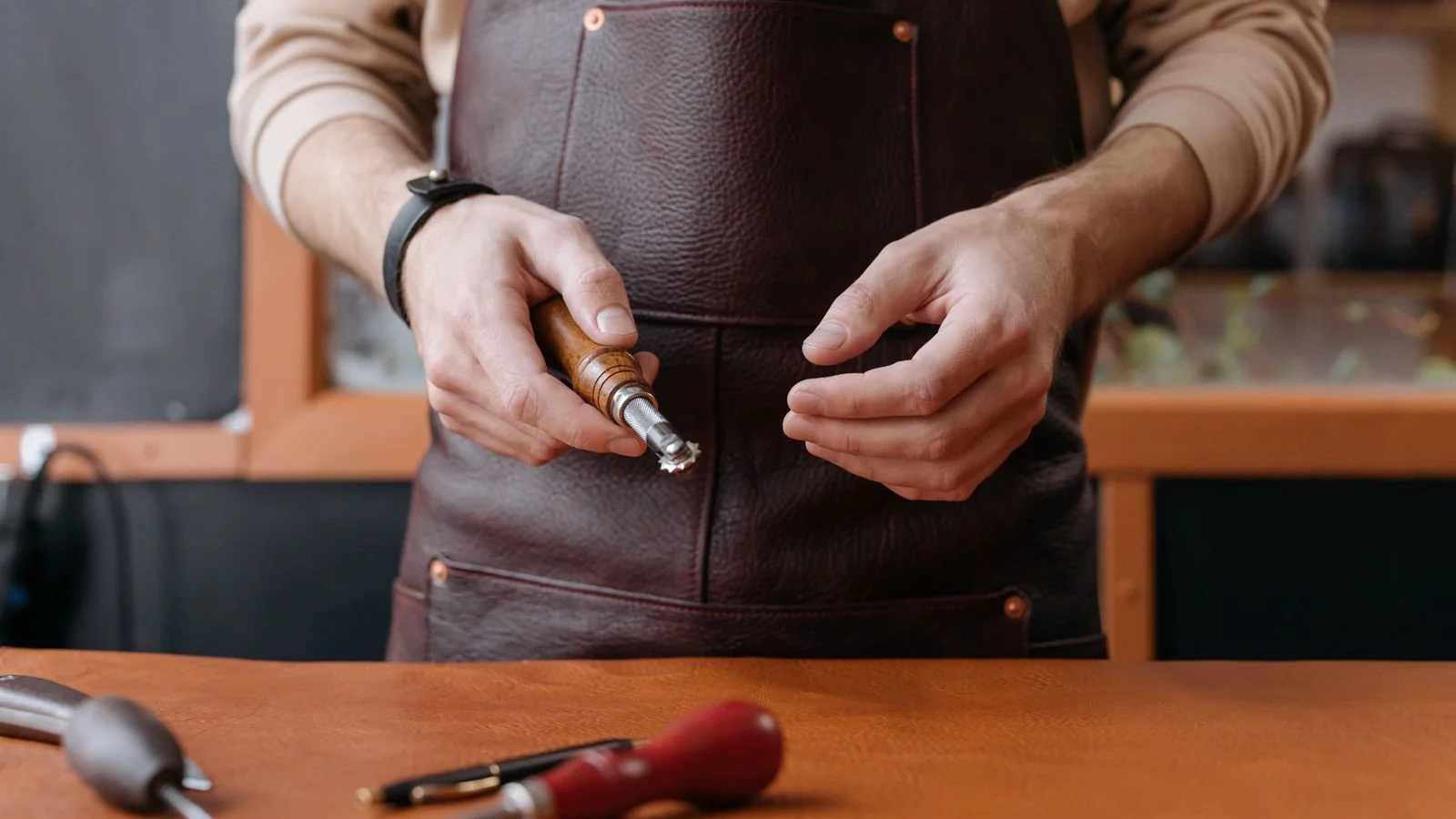 Craftsman in an apron holding a leatherworking tool, the kind of American maker Martha Stewart celebrates