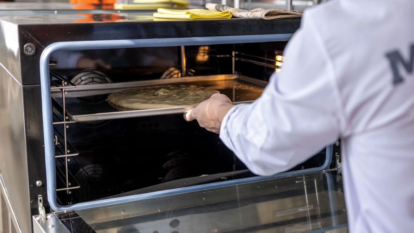 Chef sliding a pizza into an industrial oven, the kind of high-heat test Serious Eats runs on pizza ovens