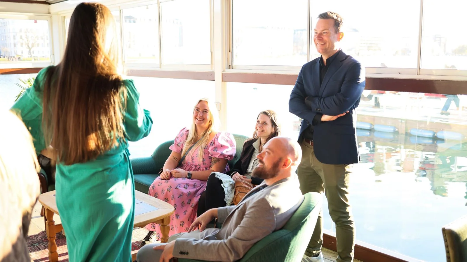 Adults in relaxed conversation in a bright room overlooking water, the executive network TNW Council is built around
