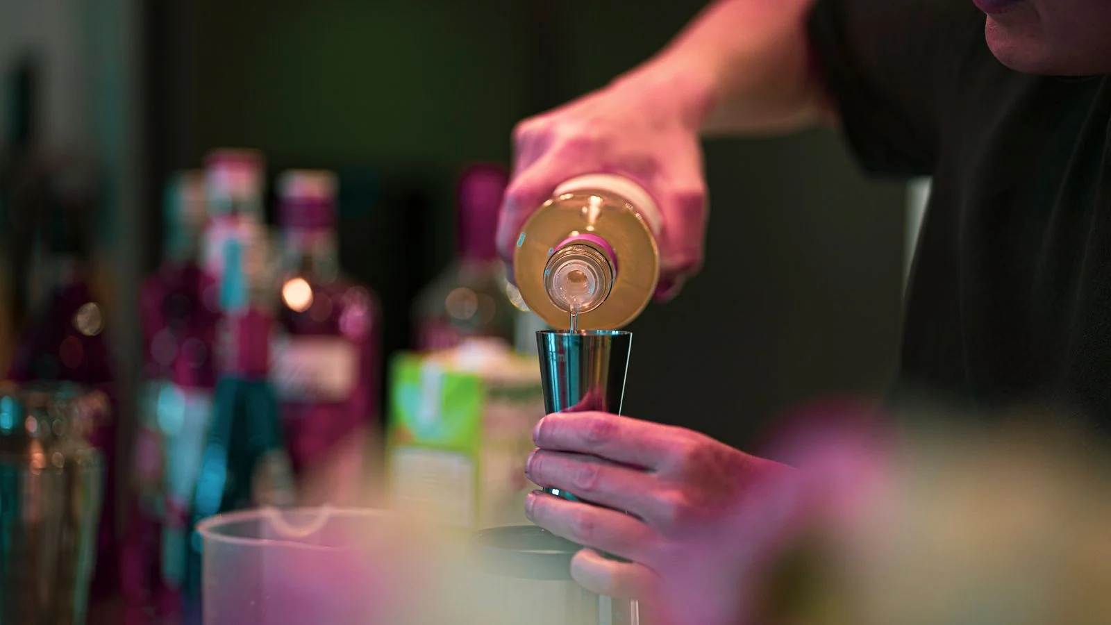 Bartender pouring a measured pour into a jigger behind a bar, the drinks coverage Thrillist used to run