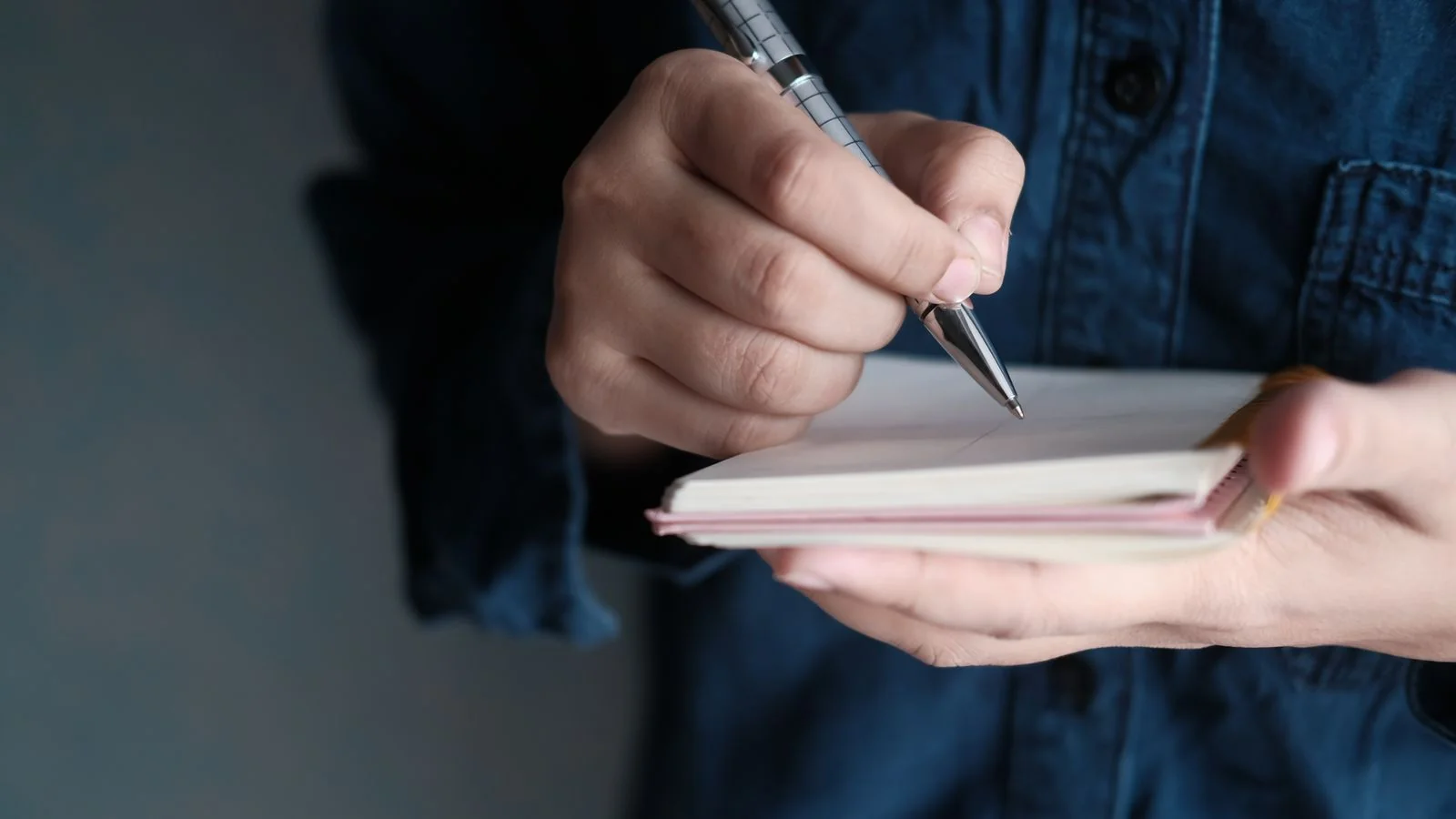 Hands writing notes in a paper notebook, researching a Thrillist writer before pitching