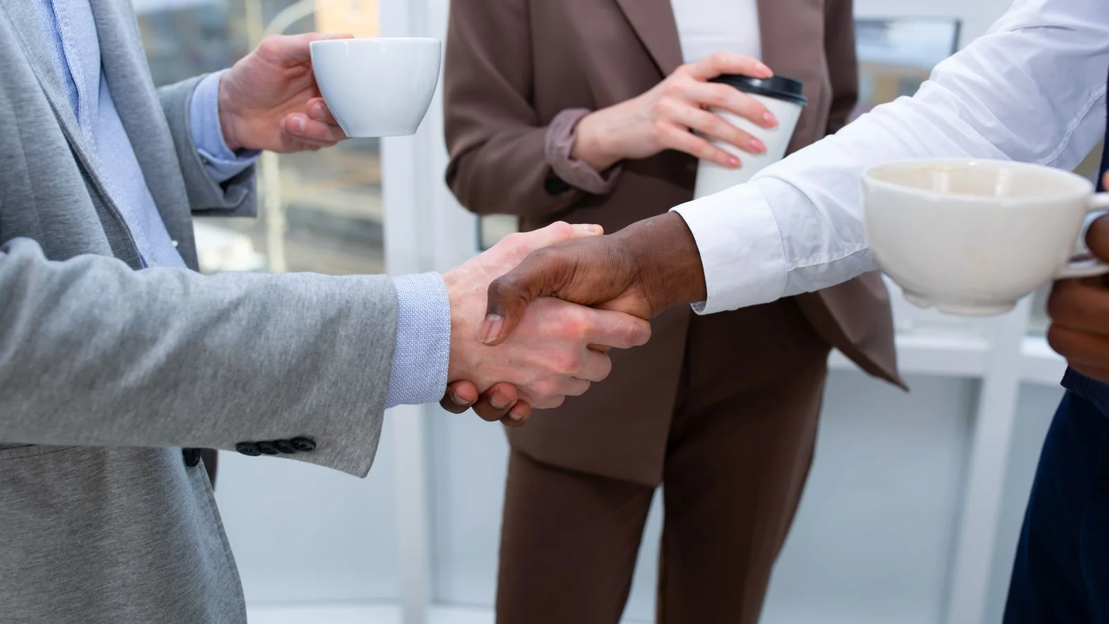 Two professionals shaking hands over coffee, the relationship layer that drives most invitations