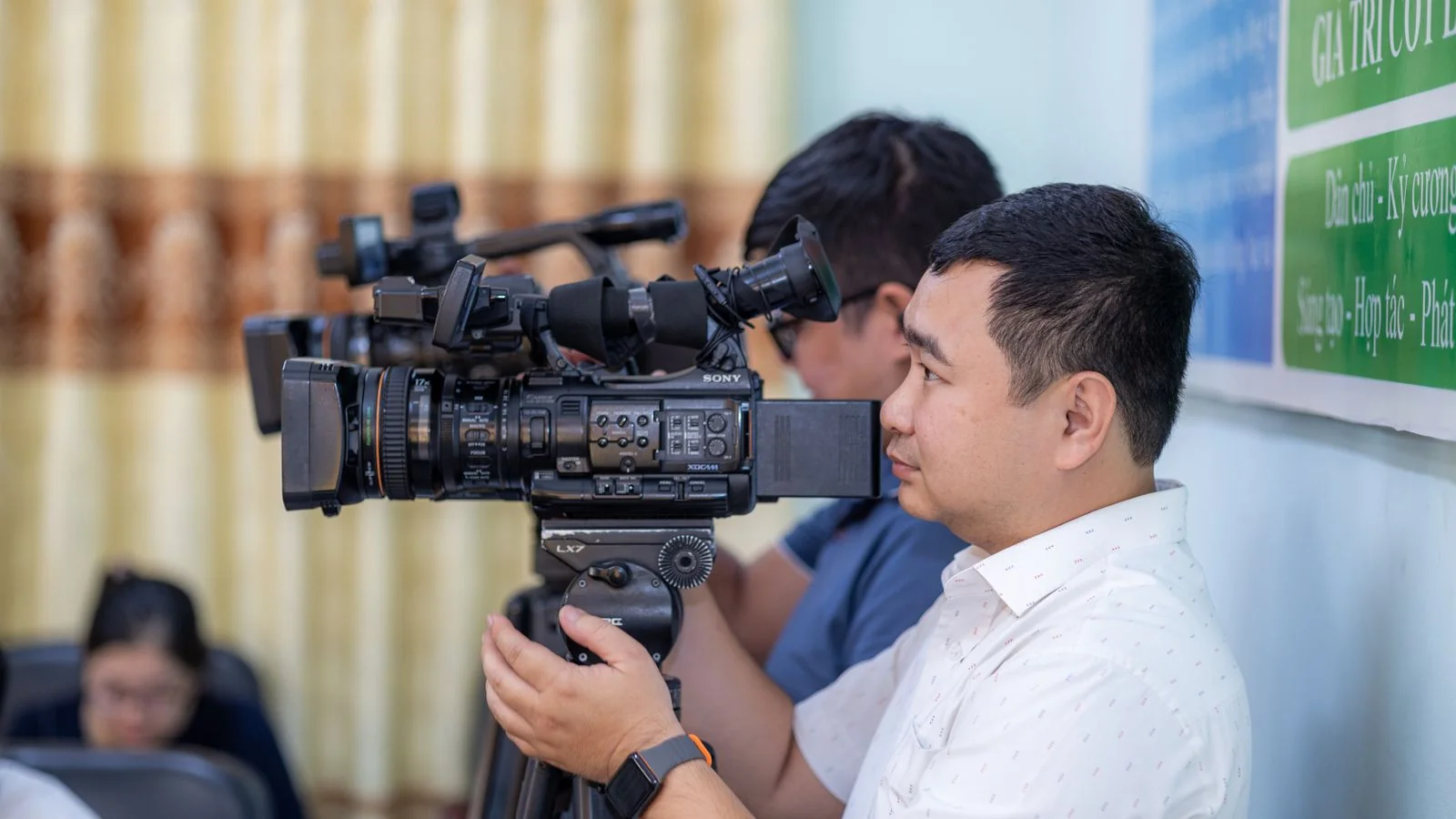 A camera operator shooting an indoor event, the visual proof a television assignment desk needs
