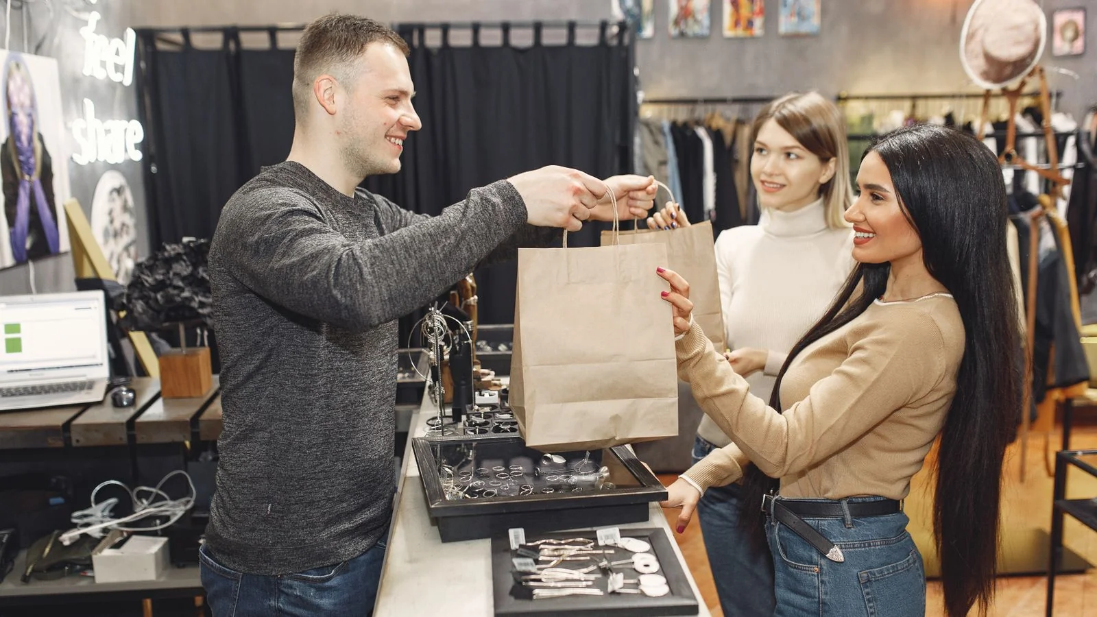 Cheerful shop assistant handing paper bags across the counter to a customer at the end of a purchase