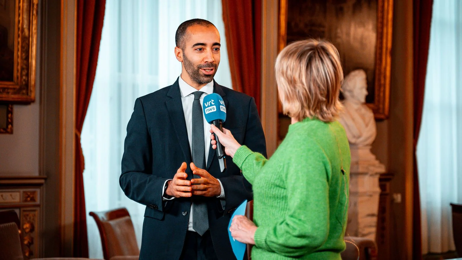 A journalist interviewing a guest in a formal setting, recorder in hand