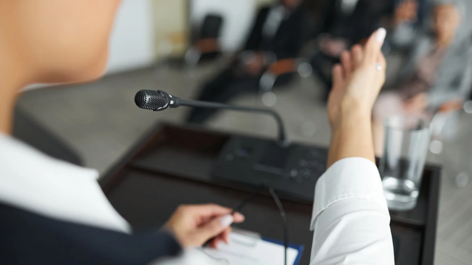 A speaker addresses a panel meeting at a podium with a microphone, the kind of setting that builds the receipts a conference programmer wants to see