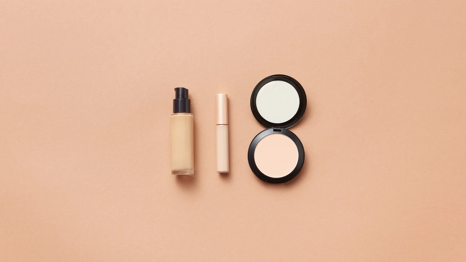 A flatlay of foundation, concealer, and powder on a beige background for a beauty feature