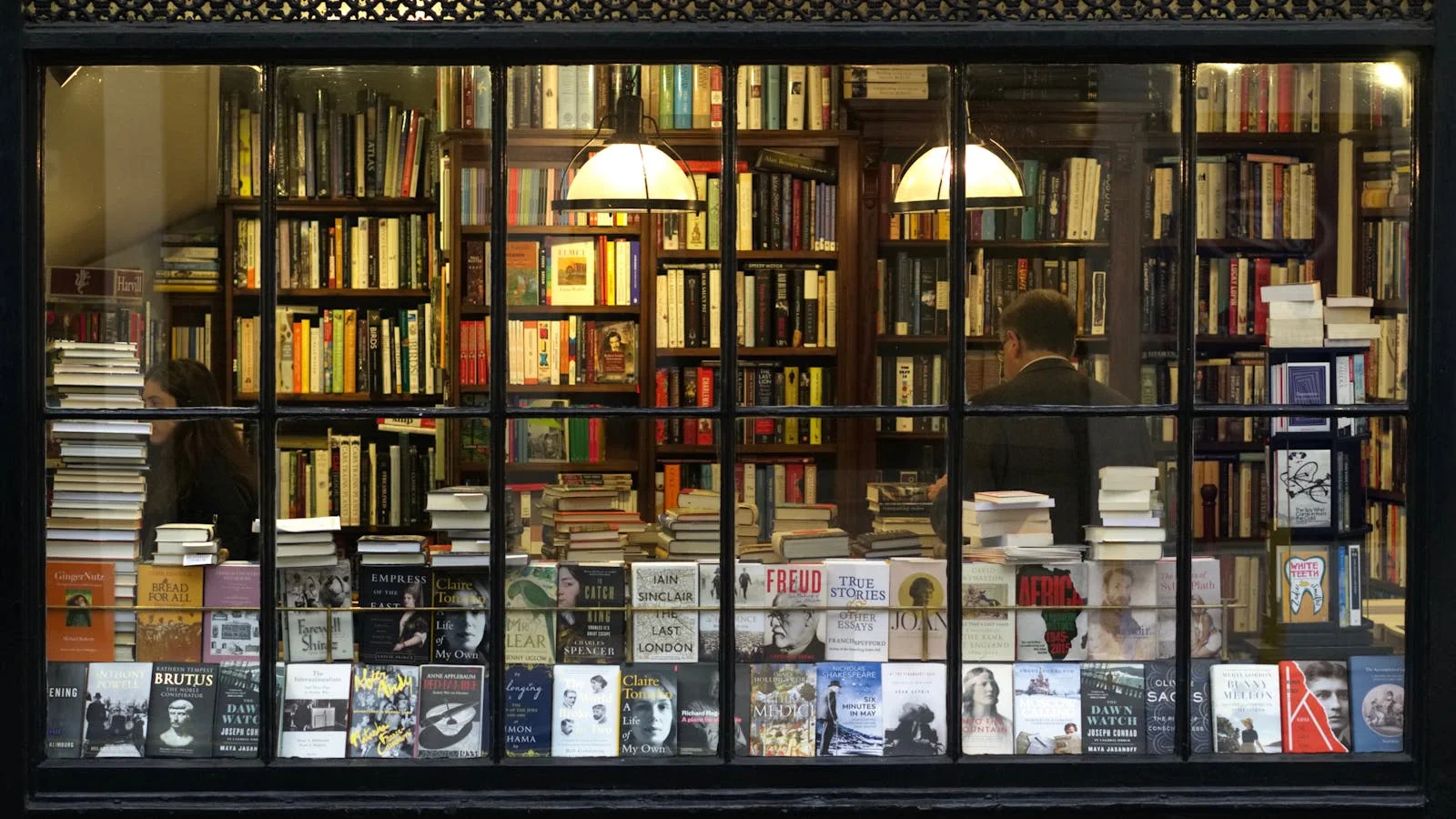 A bookstore window display of titles set out for new releases, a quiet street reflected in the glass.