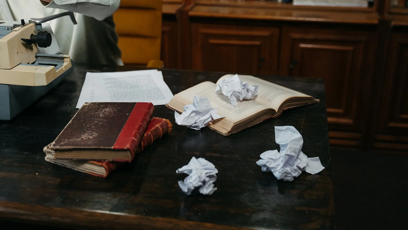 A typewriter on a wooden desk with crumpled drafts and an open notebook, the kind of working scene that gets photographed for local-author features.