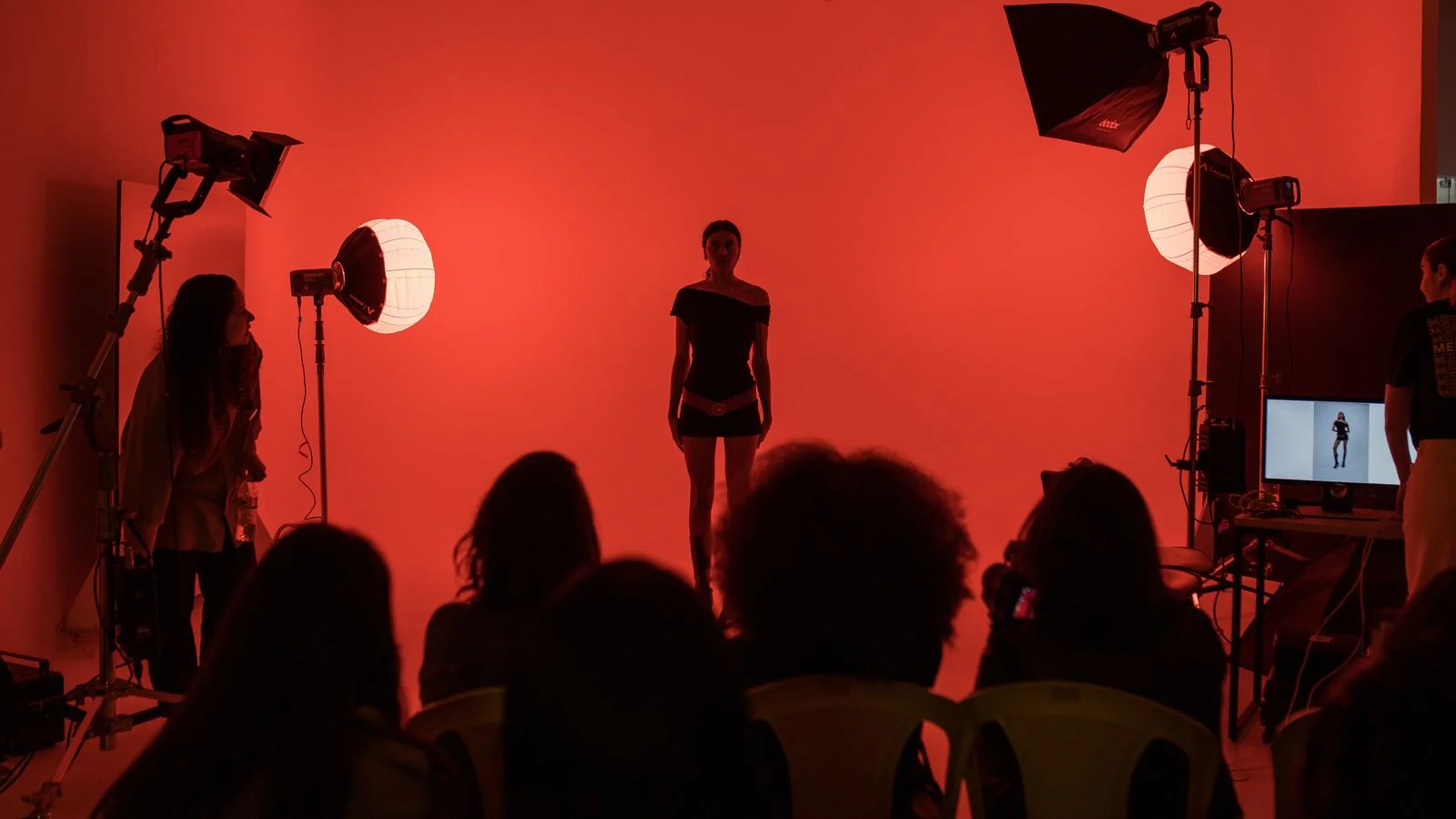 A fashion model posing under dramatic red studio lighting during a press shoot