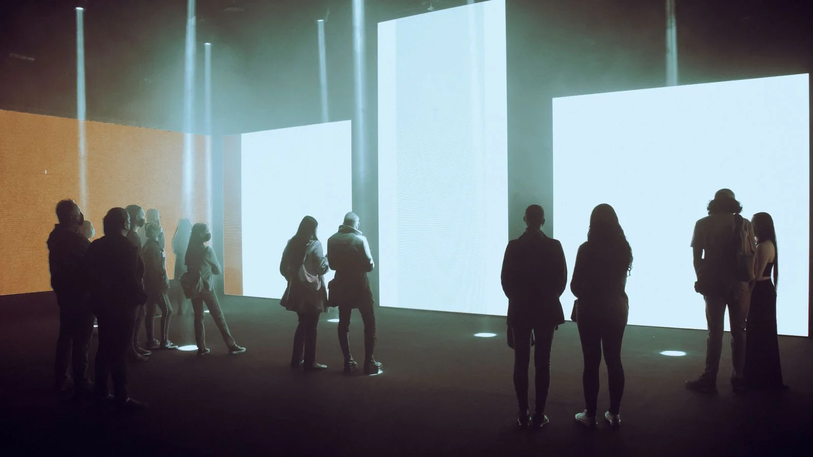 Visitors moving through an immersive exhibition hall surrounded by large illuminated digital screens