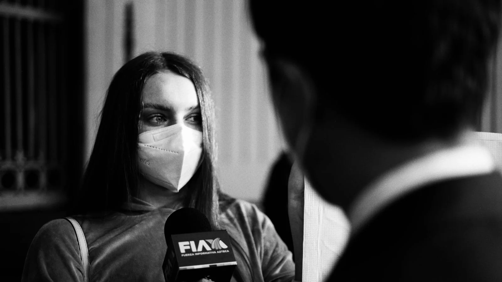 A person being interviewed on camera in a monochrome setting.