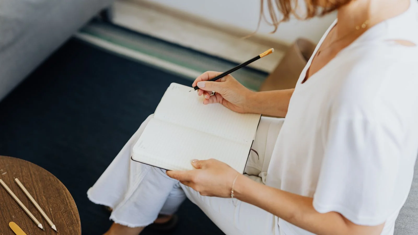 A woman writing notes in a notebook on a sofa, the way a reporter works a story between deadlines.