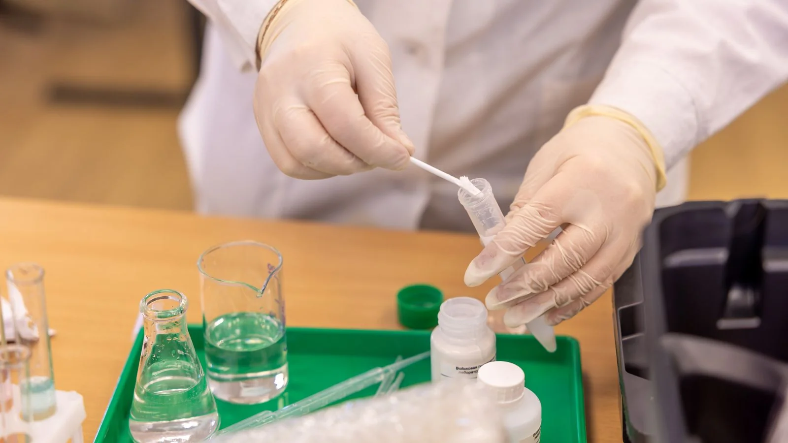 A scientist in gloves handling test tubes in a laboratory, the analysis that turns a public sample into a story.