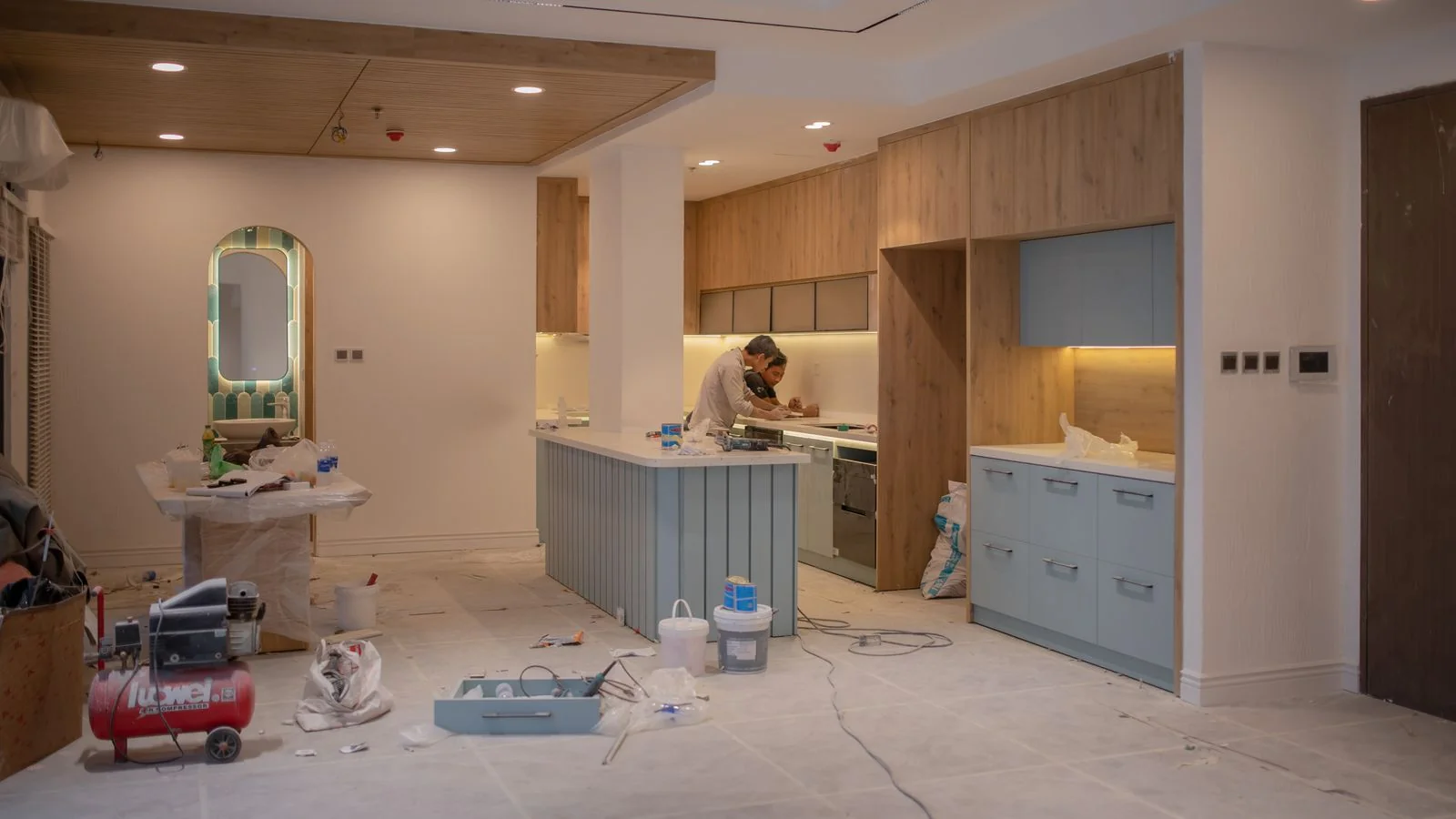 A worker mid-renovation in a kitchen surrounded by tools and materials.