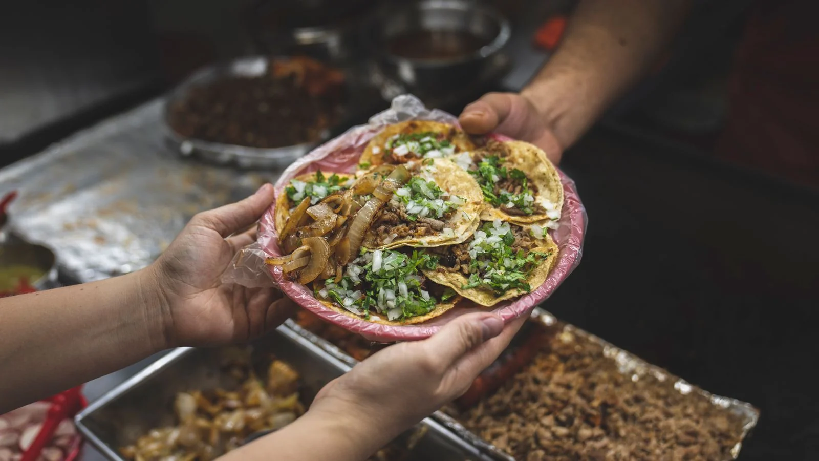 Freshly made street tacos being handed over by a vendor, the product that brings people back after the story brings them in.