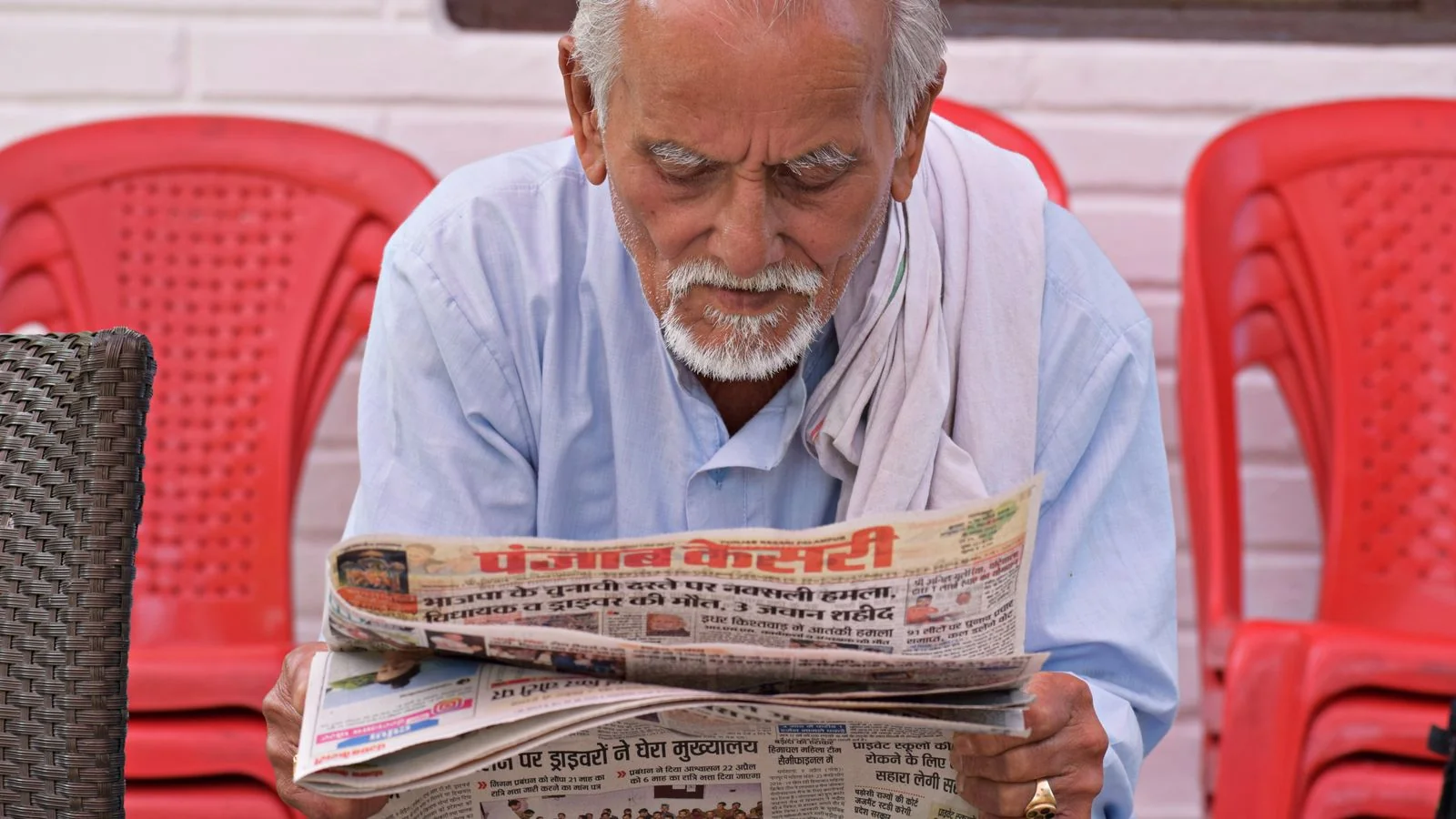 An older man reading a printed local newspaper outdoors, the community readership salon coverage actually reaches