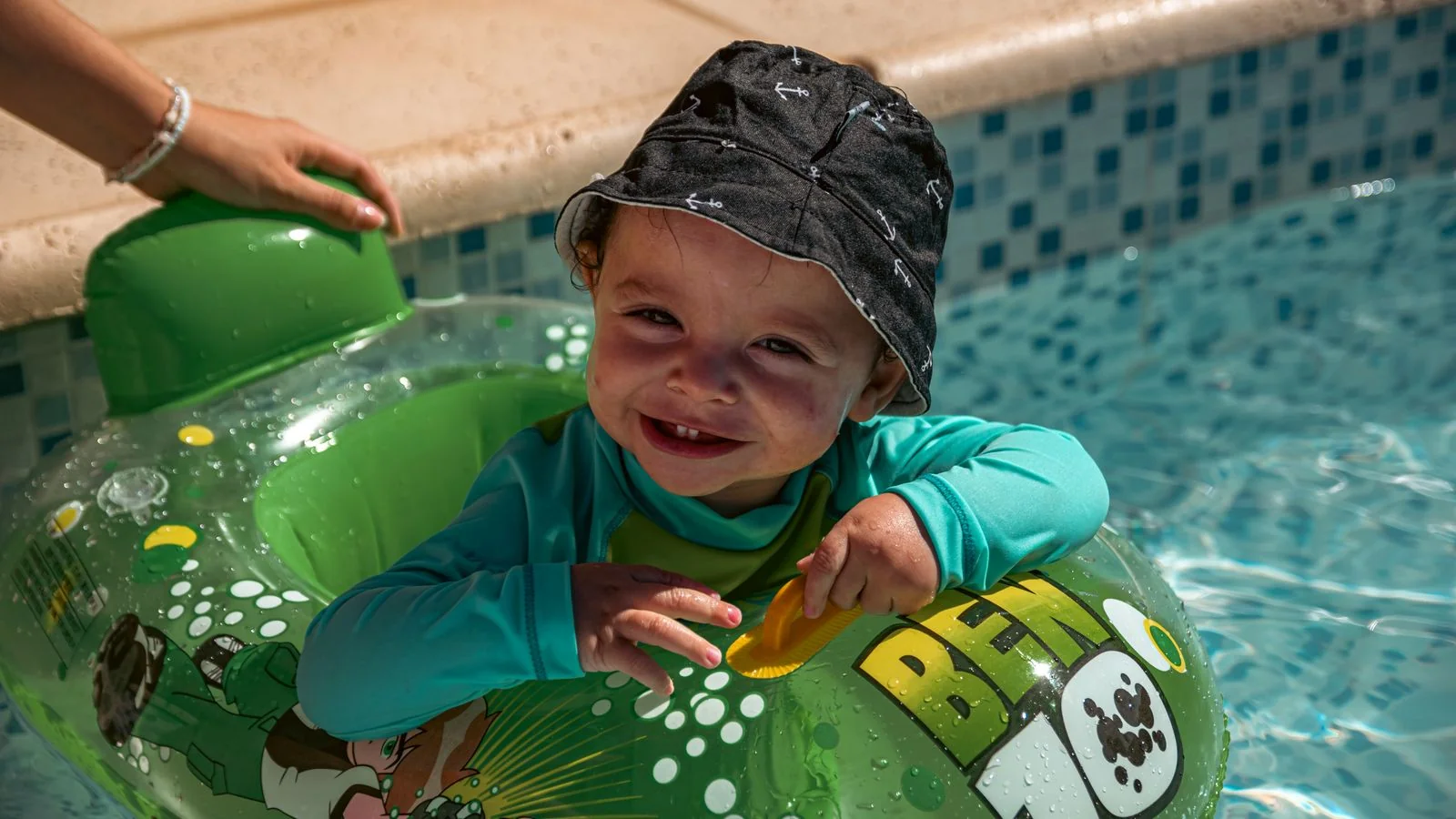 A young child in a sun hat playing with a float in the shallow end