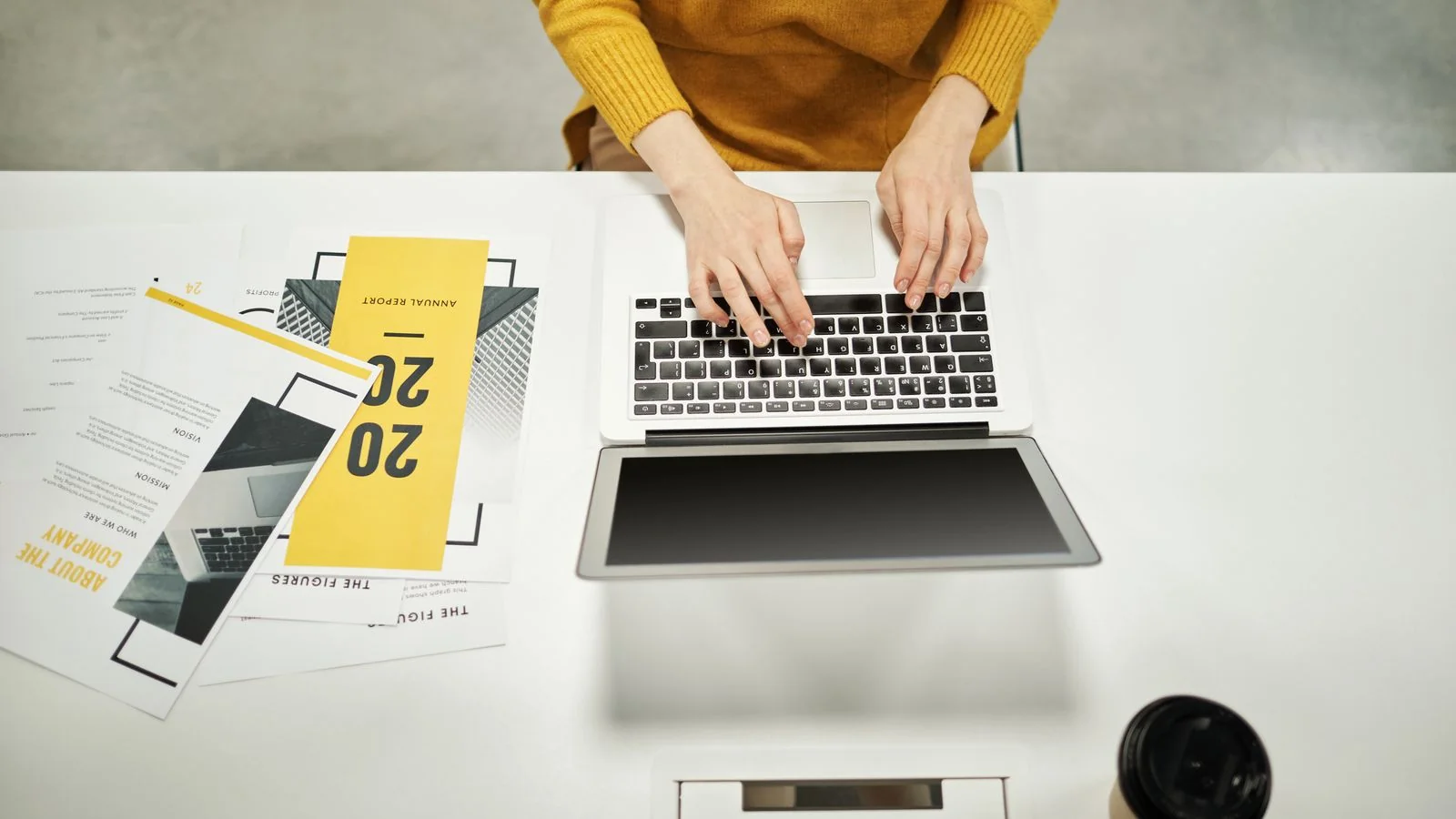 A person in a yellow sweater working on a laptop at a clean office desk.