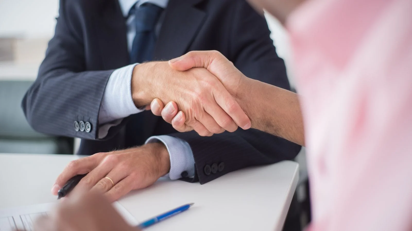 Two people shaking hands across a table in a local business setting.