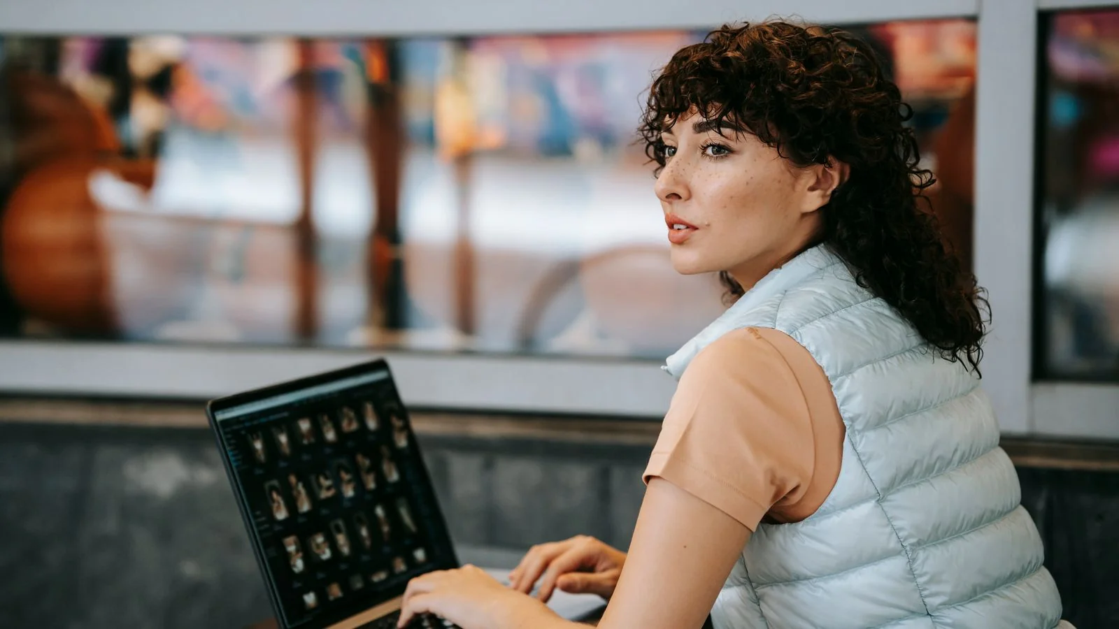 A freelance writer working from a cafe table with a photo gallery open on a laptop, the person your pitch is competing for.